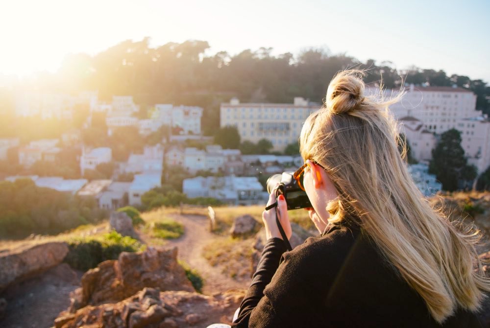 a blonde woman photographing the sun on a hill