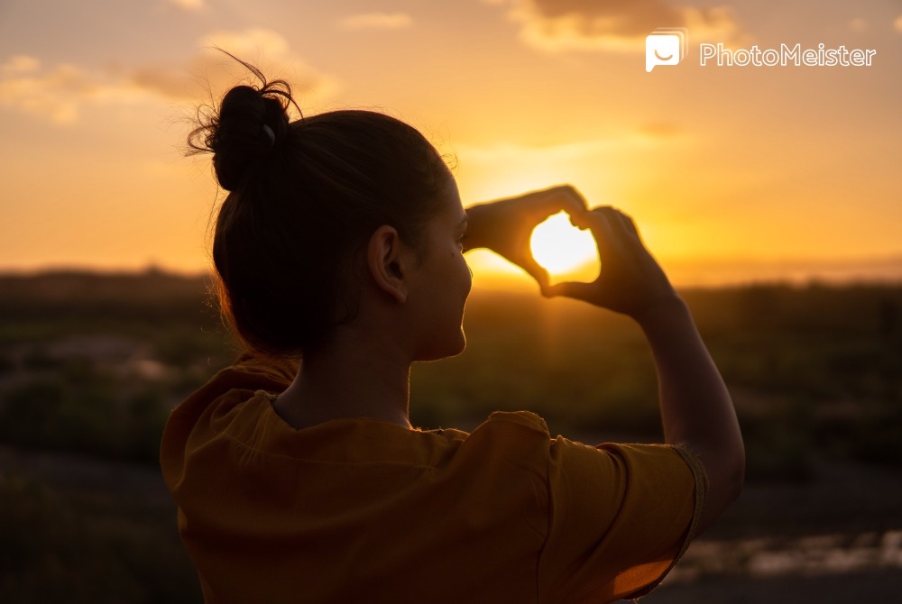 a man makes a heart with her hands around the sunset