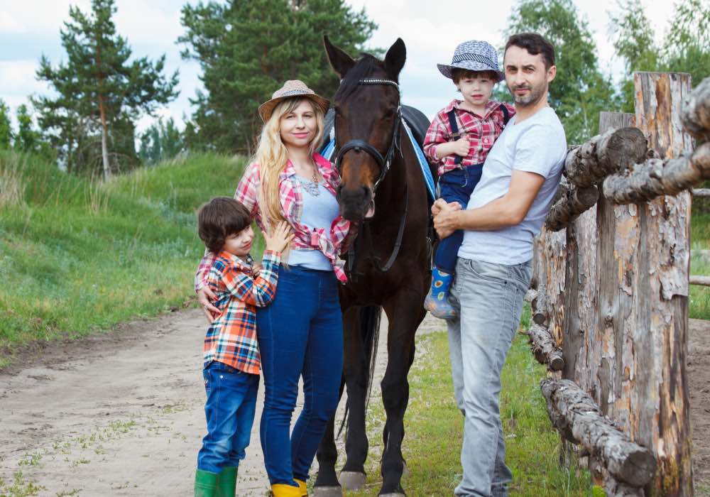 A family of two kids, mom and dad standing with a horse on a rural road, next to a wooden fence.