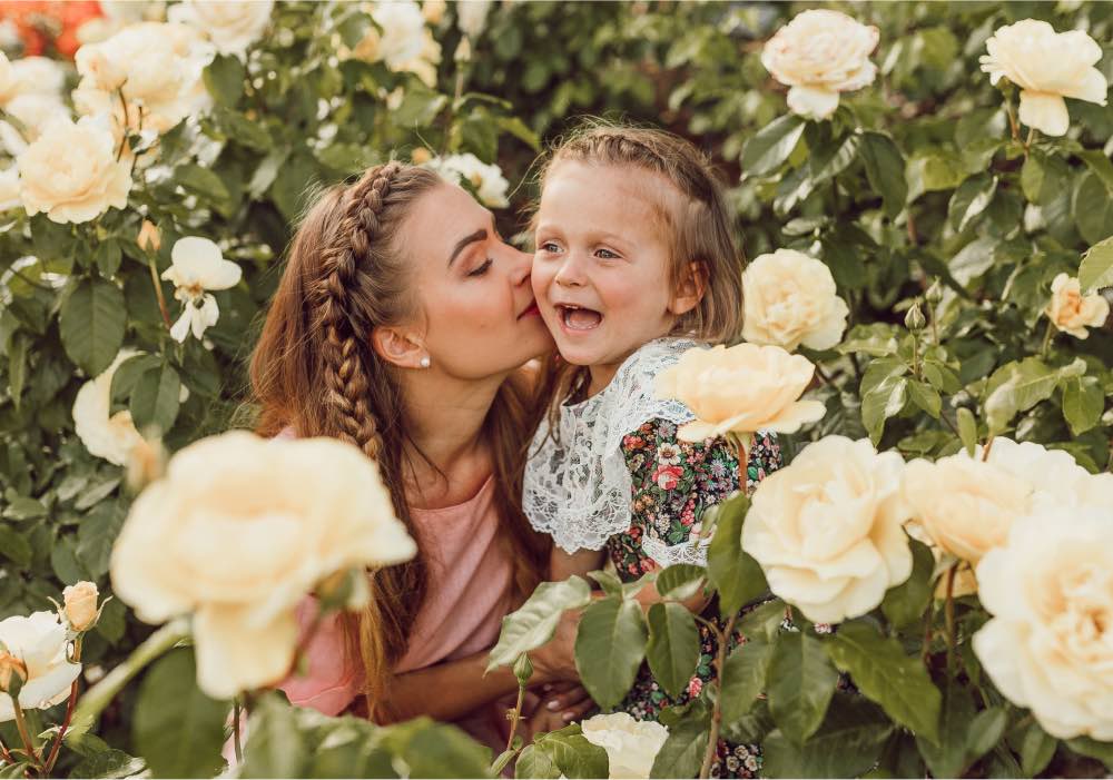 Mom and daughter in a field of flowers. Mom is giving her daughter a kiss on a cheek.
